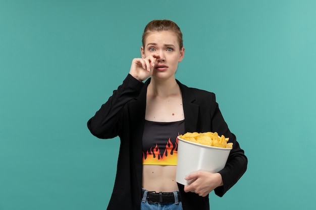 Vordere Ansicht junge Frau, die Chips hält und isst, die Film auf blauem Schreibtisch ansehen