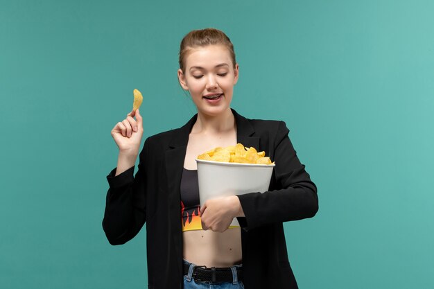 Vordere Ansicht junge Frau, die Chips hält und isst, die Film auf blauem Schreibtisch ansehen