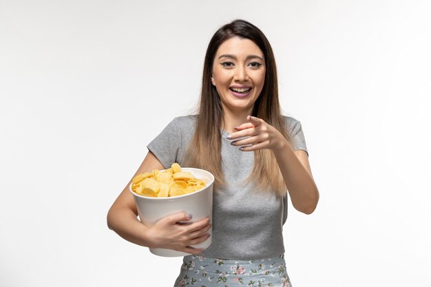 Vordere Ansicht junge Frau, die Kartoffelchips hält, während Film lachend auf weißer Oberfläche