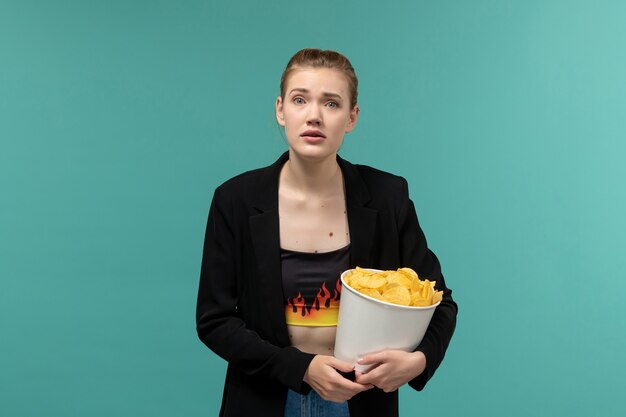 Vordere Ansicht junge Frau, die Kartoffelchips isst, die Film auf der blauen Oberfläche sehen