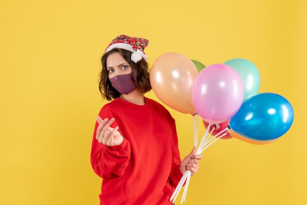 Vordere Ansicht junge Frau, die Luftballons in der Maske auf gelber Feierparty-Emotion Neujahrsfarbe hält