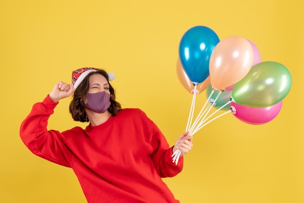 Vordere Ansicht junge Frau, die Luftballons in der sterilen Maske auf Gelb hält