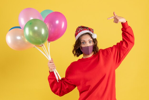 Vordere Ansicht junge Frau, die Luftballons in der sterilen Maske auf Gelb hält