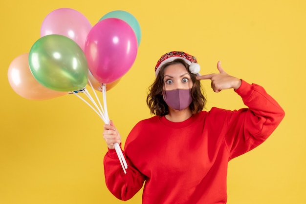 Vordere Ansicht junge Frau, die Luftballons in der sterilen Maske auf Gelb hält