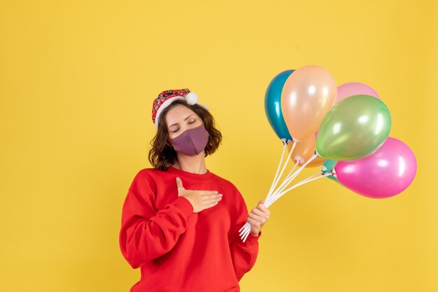 Vordere Ansicht junge Frau, die Luftballons in der sterilen Maske auf Gelb hält
