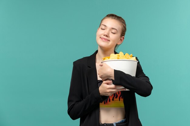 Vordere Ansicht junge Frau, die Paket mit Chips und Film auf hellblauer Oberfläche hält