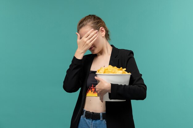 Vordere Ansicht junge Frau, die Paket mit Kartoffelchips hält und Film auf der blauen Oberfläche sieht