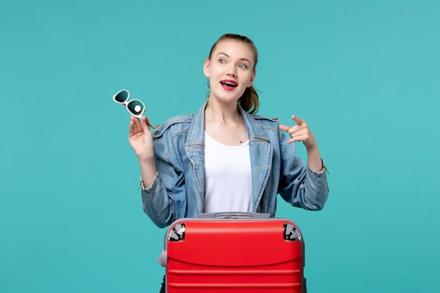 Vordere Ansicht junge Frau, die Sonnenbrille hält und sich auf Urlaub auf dem blauen Raum vorbereitet