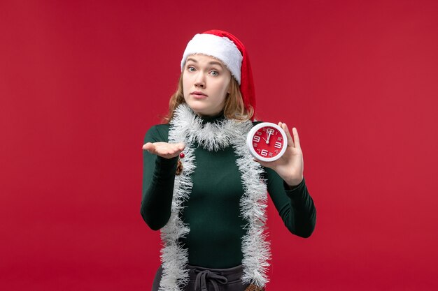 Vordere Ansicht junge Frau, die Uhr auf rotem Boden Neujahrsweihnachtsferien hält