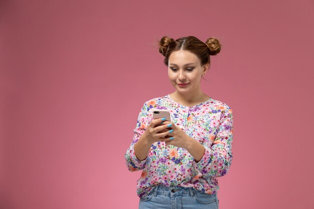 Vordere ansicht junge frau in blume entworfenes hemd und blaue jeans unter verwendung eines telefons auf dem rosa hintergrund