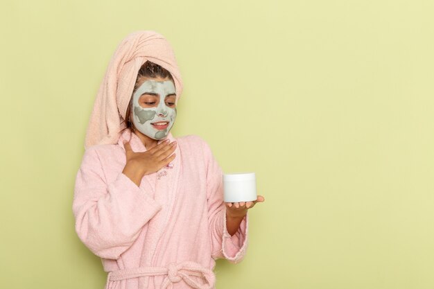 Vordere Ansicht junge Frau nach Dusche im rosa Bademantel, der Creme auf grüner Oberfläche hält