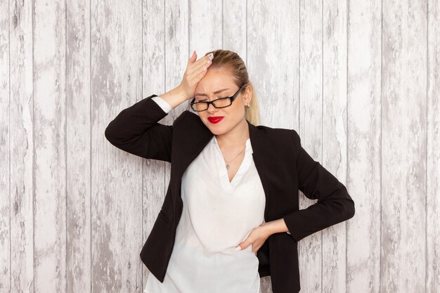 Vordere Ansicht junge Geschäftsfrau in strenger Kleidung schwarze Jacke mit optischer Sonnenbrille, die auf der weißen Schreibtischarbeitsjobbüro-Geschäftsfrau Dame aufwirft