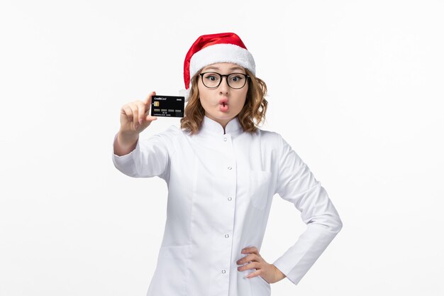 Vordere Ansicht junge Ärztin, die Bankkarte auf weißem Schreibtischfeiertagskrankenschwester neues Jahr hält