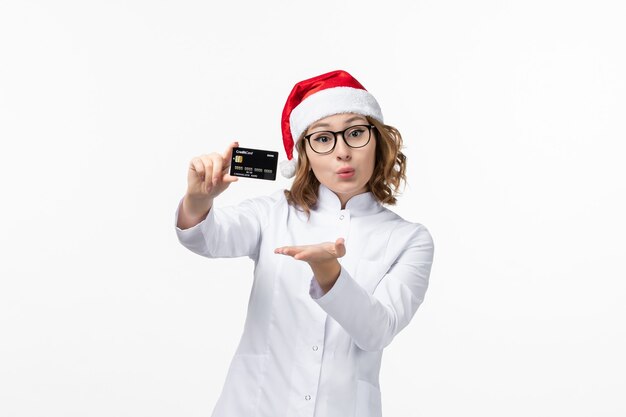 Vordere Ansicht junge Ärztin, die Bankkarte auf weißem Wandfeiertagskrankenschwester Neujahr hält