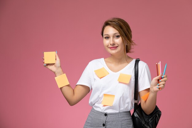 Vordere Ansicht junge Studentin im weißen T-Shirt lächelnd hält Bleistifte auf rosa Hintergrund Lektion Universität College-Studienbücher