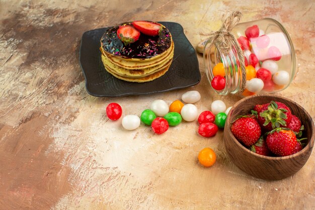 Vordere Ansicht süße Pfannkuchen mit bunten Bonbons auf hölzernem Schreibtischkuchen-Nachtisch süßer Kuchen