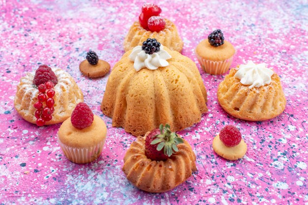 Vordere nähere Ansicht gebackene leckere Kuchen mit Sahne zusammen mit Beeren auf hellviolettem Schreibtisch