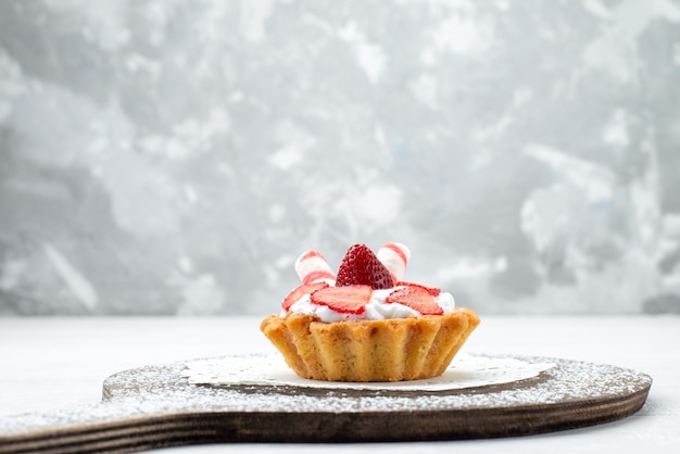 Vordere nähere Ansicht kleiner leckerer Kuchen mit Sahne und geschnittenen Erdbeeren auf Weiß