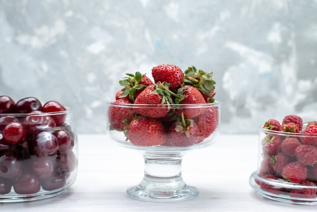 Vordere nähere Ansicht rote Sauerkirschen frisch ganz und weich mit Erdbeeren und Himbeeren auf hellem Schreibtisch