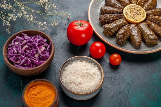 Vordere Nahansicht Blatt Dolma köstliche östliche Fleischmahlzeit in grünen Blättern mit Tomaten und Gewürzen auf blauem Schreibtisch gerollt