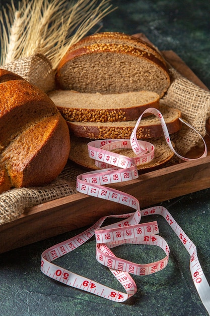 Vordere Nahansicht des Ganzen und frisches Schwarzbrot auf Handtuch in einem braunen Holztablettmesser auf dunkler Mischfarbenoberfläche schneiden