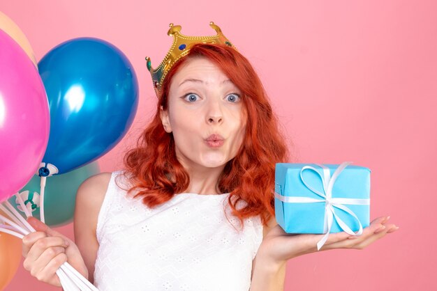 Vordere Nahansicht junge Frau, die bunte Luftballons hält und auf dem Rosa präsentiert