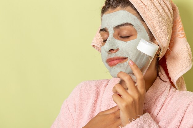 Vordere Nahansicht junge Frau nach der Dusche im rosa Bademantel, der Make-up-Entferner auf grüner Oberfläche hält