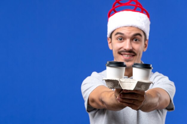 Vordere Nahansicht junger Mann, der Kaffeetassen auf blauem Wandgefühl männlichem Neujahr hält