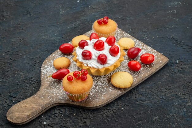 Vordere Nahansicht kleine leckere Kuchen mit Sahne und frischen Früchten auf der dunklen Oberfläche süße Kekse Kuchen Dessert Fruchtbeere