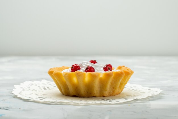 Vordere Nahansicht kleiner köstlicher Kuchen mit Sahne und roten Preiselbeeren lokalisiert auf der leichten Oberfläche süßer Tee