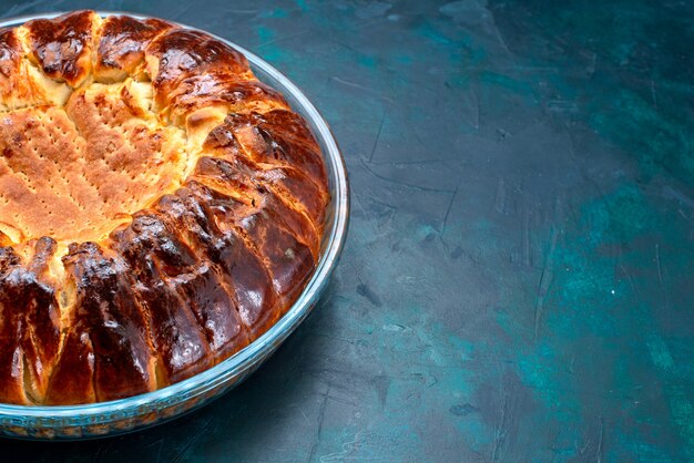 Vordere Nahansicht köstliche gebackene Kuchenrunde geformte süße innere Glaspfanne auf hellblauem Hintergrund.