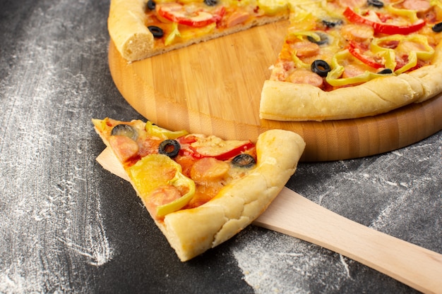 Vordere Nahansicht leckere käsige Pizza mit roten Tomaten, schwarzen Oliven, Paprika und Würstchen