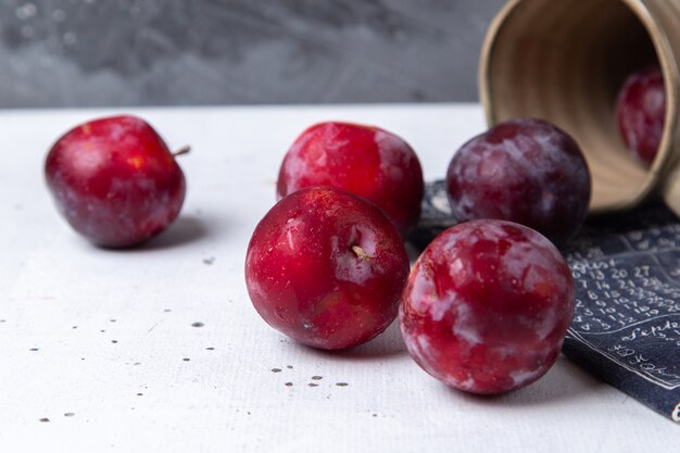 Vordere Nahansicht rote saure Pflaumen frisch und reif überall auf dem weißen Schreibtisch