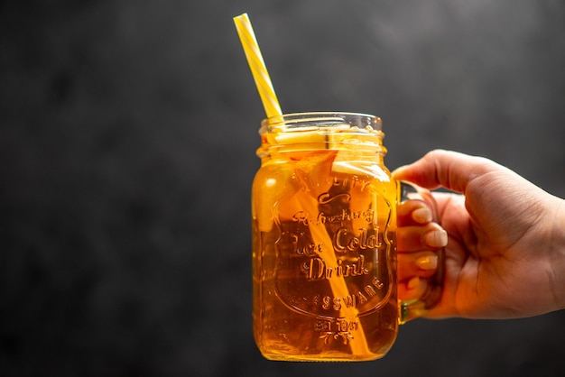 Vordere Nahaufnahme der Hand, die ein Glas frischen natürlichen köstlichen Saftes mit einer Röhre darin auf schwarzem Hintergrund hält