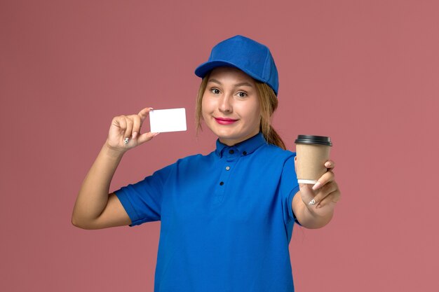 Vorderer Blick junger weiblicher Kurier in der blauen Uniform, die das Halten der Tasse Kaffee und der weißen Karte, Dienstuniformfrau-Jobarbeiter aufwirft