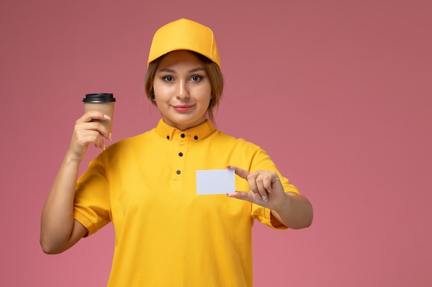 Vorderer Blick weiblicher Kurier in gelbem einheitlichem gelbem Umhang, der weiße Karte und Kaffee auf dem rosa Hintergrunduniformlieferauftrag hält