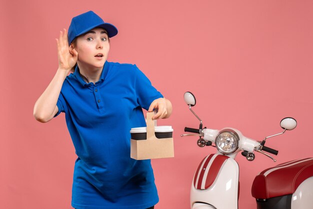 Vorderer Blick weiblicher Kurier mit Lieferkaffee auf rosa Fahrradarbeitslieferdienstarbeiterfrauenuniformjob