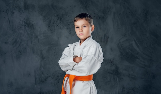 Vorschuljunge in einem weißen Karate-Kimono mit orangefarbenem Gürtel.