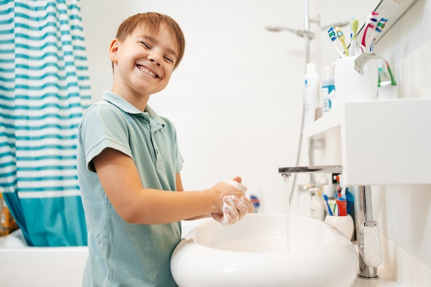 Kostenloses Foto vorschullächelnder junge händewaschen mit seife unter dem wasserhahn mit wasser.