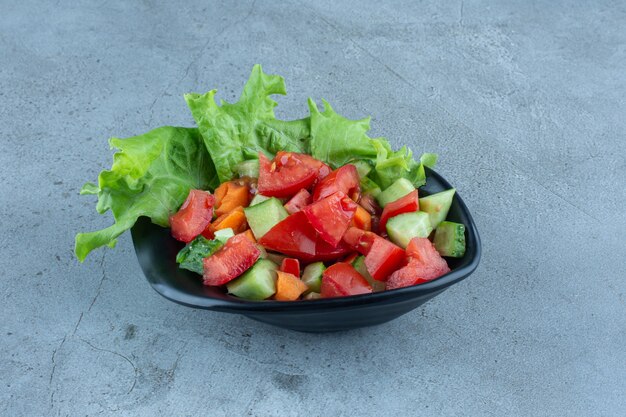 Vorspeisenschale mit Gurken-, Tomaten- und Karottenscheiben mit Salatblatt auf Marmor.