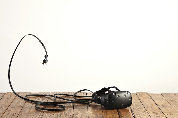 VR-Headset und einige Kabel auf rauem rustikalem Holztisch an weißer Wand