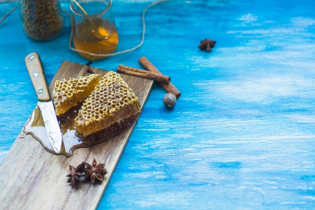 Wabenstücke mit Gewürzen; Bienenpollen Glas; Messer und Honigtopf auf blauem Hintergrund