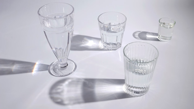 Wässern Sie in der unterschiedlichen Art der Gläser mit Schatten auf weißem Hintergrund