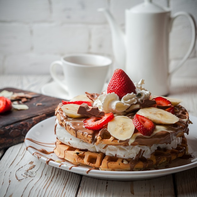 Waffeleis-Torte mit Seitenansicht mit Erdbeere und Tasse und Teekanne in rundem weißem Teller