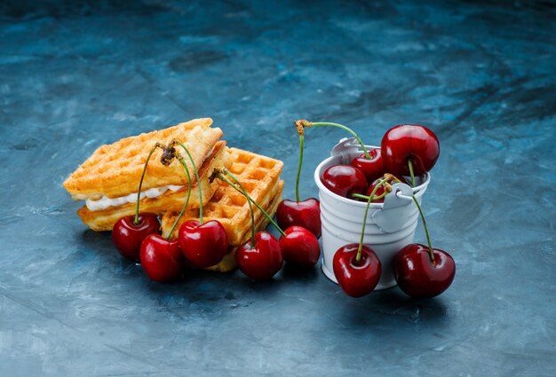 Waffeln mit kirschen-hochwinkelansicht auf einer grungy blauen oberfläche