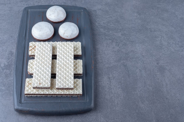 Waffeln und pop-kuchen auf einem holztablett auf marmortisch.