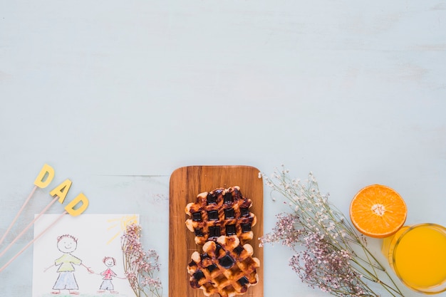 Waffeln und Saft in der Nähe von Blumen und Zeichnung