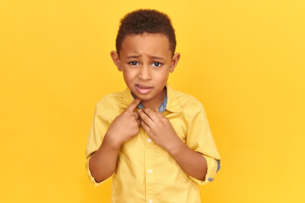 Wahre menschliche Reaktionen, Emotionen und Gefühle. Emotional verängstigter Vorschulkind in Jacke mit ängstlichem Blick, Zeigefinger auf sich selbst zeigend