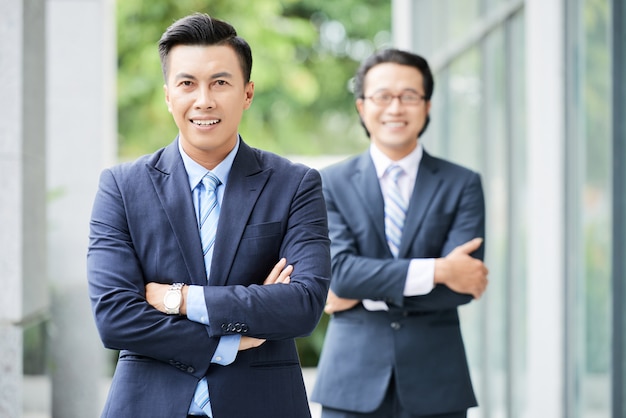 Waistup schoss von zwei asiatischen Geschäftsmännern, die mit den Armen stehen, die draußen gefaltet wurden