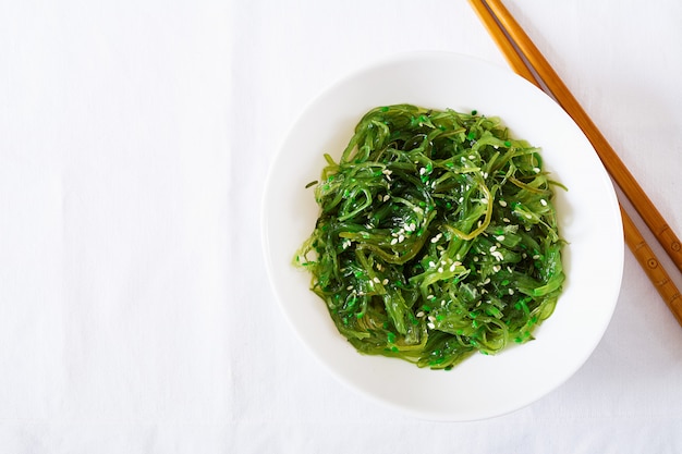 Wakame Chuka oder Algensalat mit Sesam in Schüssel auf weißem Tisch. Traditionelles japanisches Essen. Draufsicht. Flach liegen